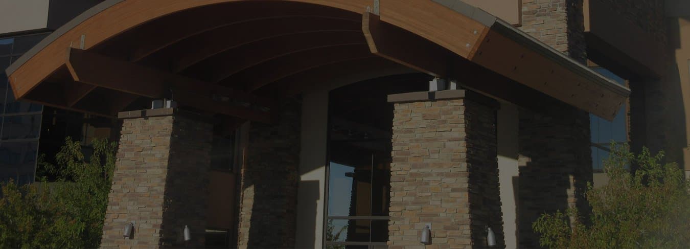 The entrance to the Hershey Decker Drake office in Lone Tree, with a curved timber canopy over stone pillars.